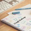 A notebook titled 75 Soft Challenge with various icons and a blue pen resting on a wooden desk.