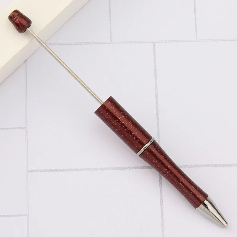 A DIY beadable pen set with a metallic silver body and a dark red, textured barrel is shown on a white surface.
