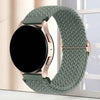 A close-up of a green knitted nylon watch strap with a rose gold buckle, displayed next to a black smartwatch.
