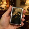 A hand holds a vintage stainless steel card and cash case featuring an antique painting of a bird.