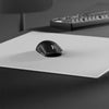 Souris ergonomique noire posée sur un tapis de souris en verre blanc sur une surface sombre.