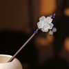 Une épingle à cheveux avec un motif floral blanc, des accents bleus et de petites perles violettes sur un bâton en bois foncé