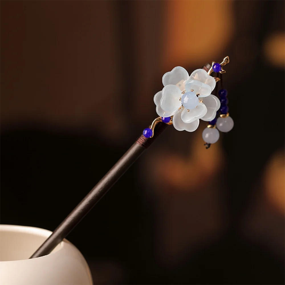 Une épingle à cheveux avec un motif floral blanc, des accents bleus et de petites perles violettes sur un bâton en bois foncé