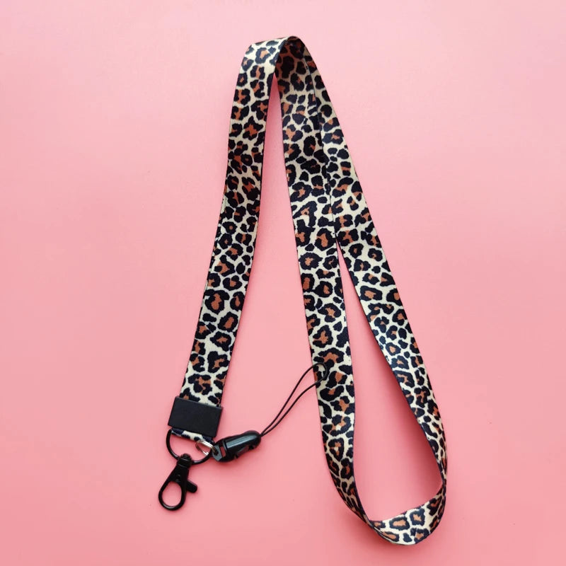 A black and brown leopard print lanyard with a black ID holder attached, displayed on a pink background.