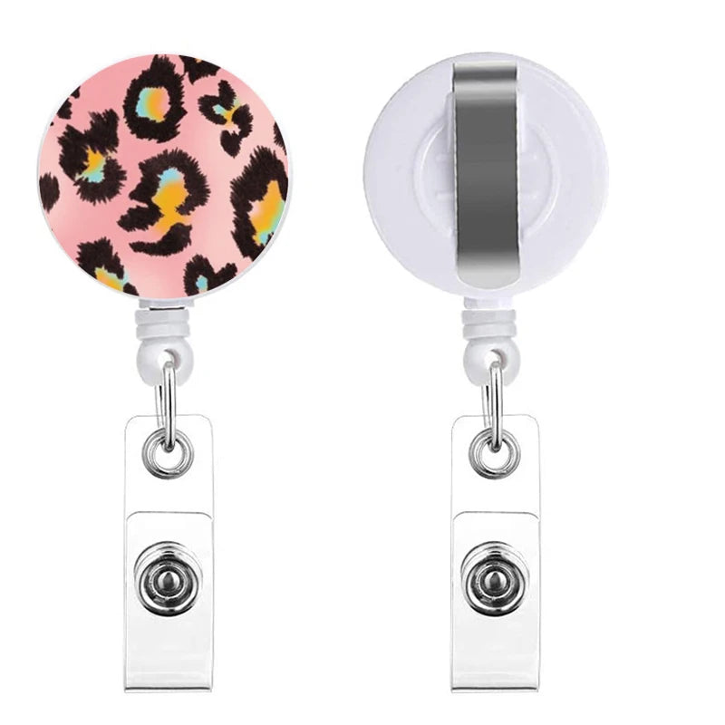 A silver retractable badge holder with a pink leopard print charm.
