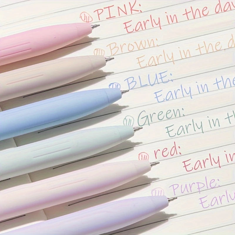 A collection of six pastel gel pens in pink, brown, blue, green, white, and purple are lined up on a sheet of paper.