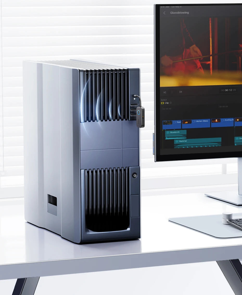 Silberner 2-in-1 Bluetooth-Audioadapter auf einem weißen Schreibtisch neben einem Computermonitor.