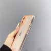 A hand holds a clear phone case with an orange rim on an iPhone, showing the back design.