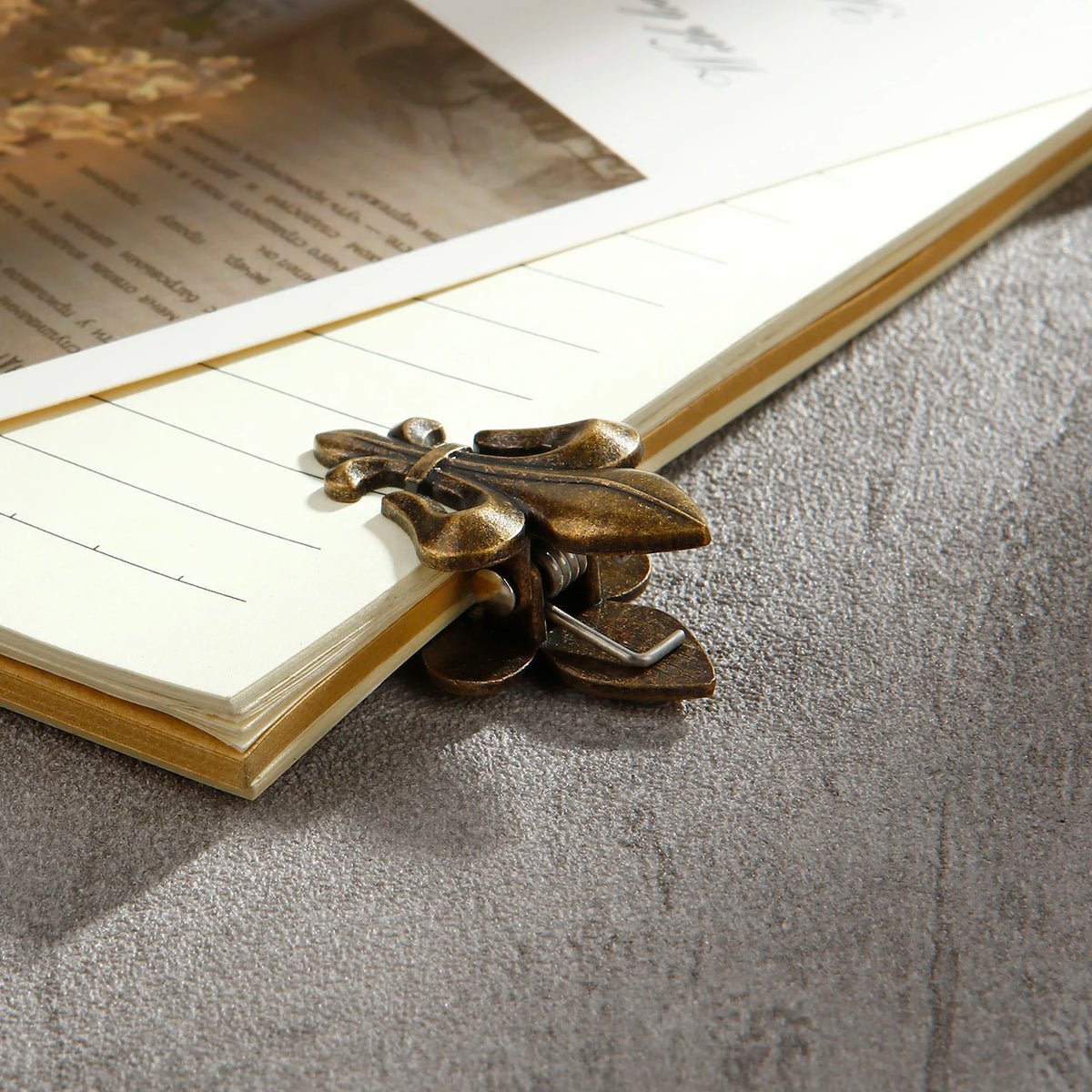 Two bronze iris-shaped metal binder clips resting on a lined paper inside a notebook.