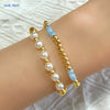 A gold-plated shell pearl beaded bracelet with white and light blue beads worn on a wrist.