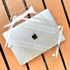 Eine klare Schutzhülle liegt auf einem silbernen MacBook Pro Laptop auf einer Holzoberfläche.