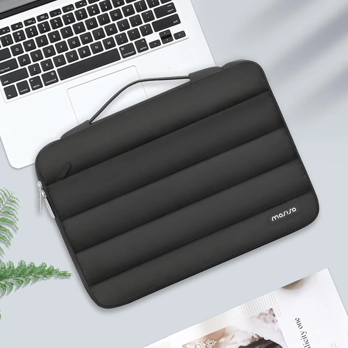 A dark gray protective laptop sleeve bag with reinforced padding resting on a light surface next to a laptop.