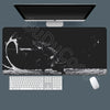 A black gaming mousepad with a white keyboard and white mouse placed beneath a computer monitor.