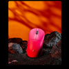 Pinke ergonomische kabellose Gaming-Maus liegt auf dunklen Felsen mit orangefarbenem Lichthintergrund.