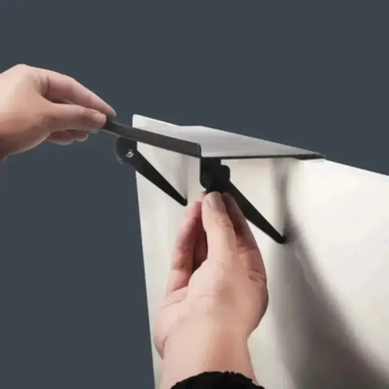 Eine Hand justiert ein schwarzes multifunktionales Regalsystem auf einer weißen Oberfläche.