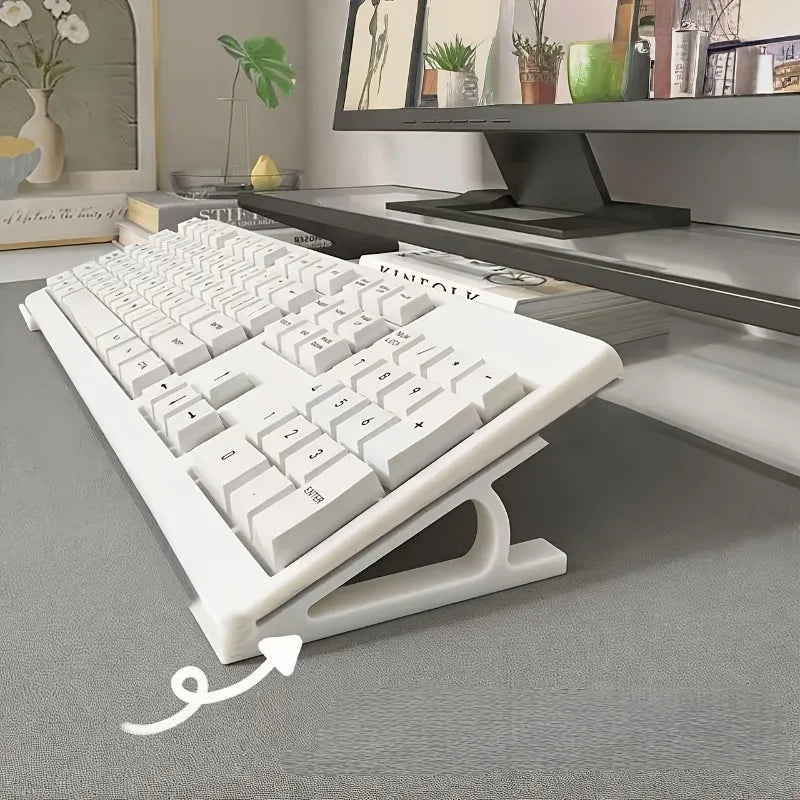 A white ergonomic keyboard riser stand with an anti-slip base is shown on a gray desk.