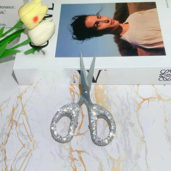 A pair of silver rhinestone crafting scissors rests on a white box with yellow flowers.
