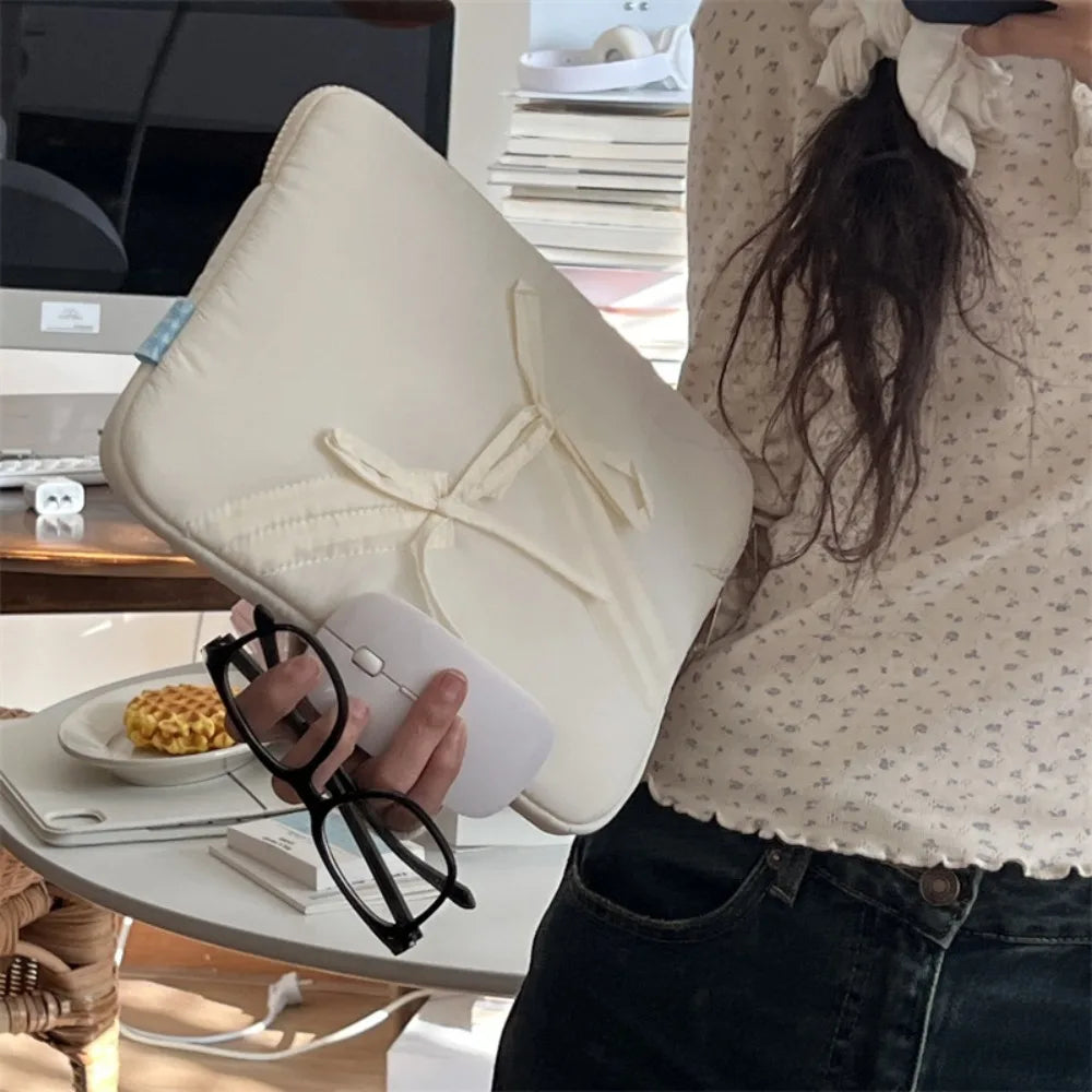 A person holds a beige laptop sleeve case, black glasses, and a laptop on a desk.