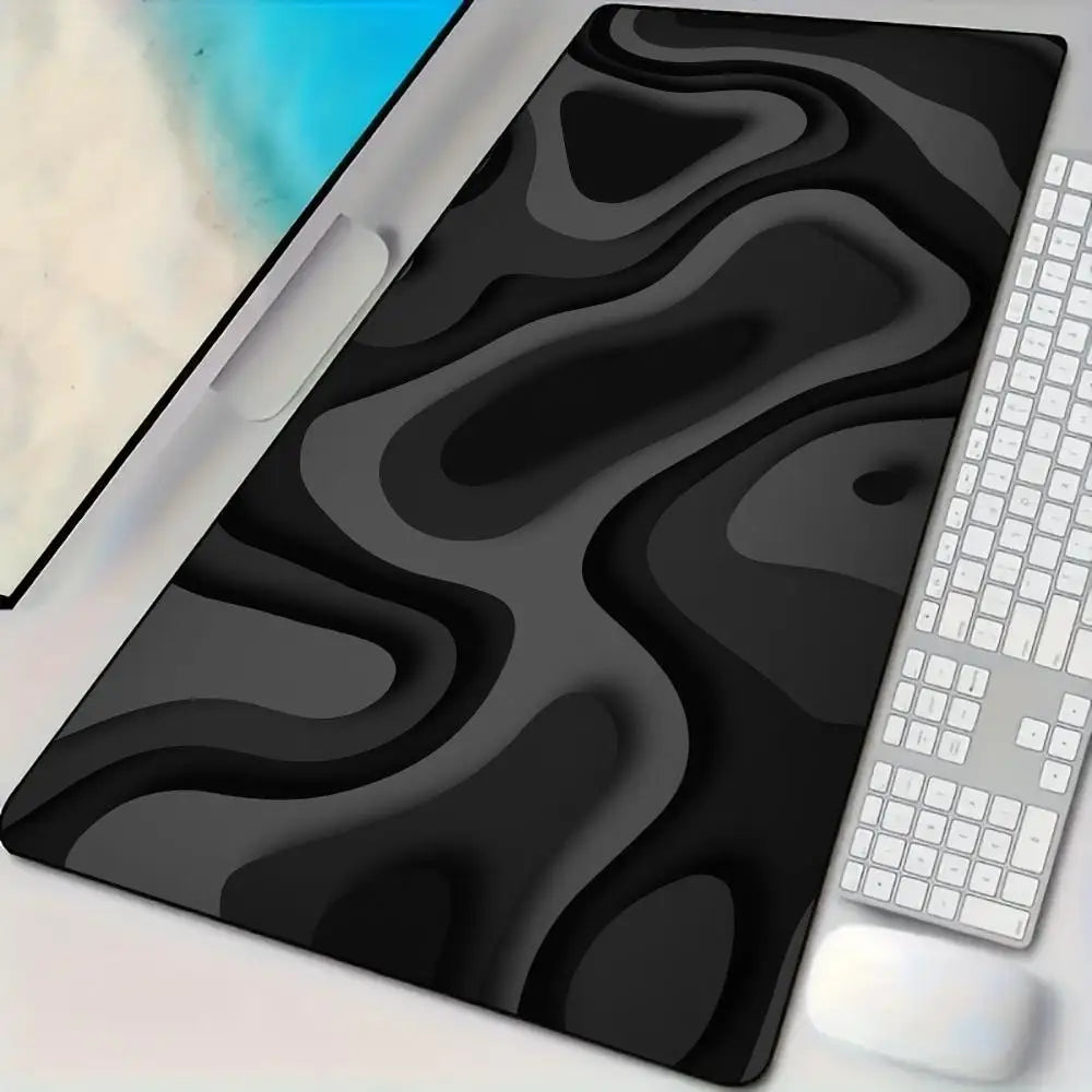 A black abstract art desk mat with a non-slip rubber base is shown next to a white keyboard and mouse.
