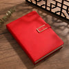 A red A5 retro leather notebook lying on a wooden surface next to a decorative wooden shelf.