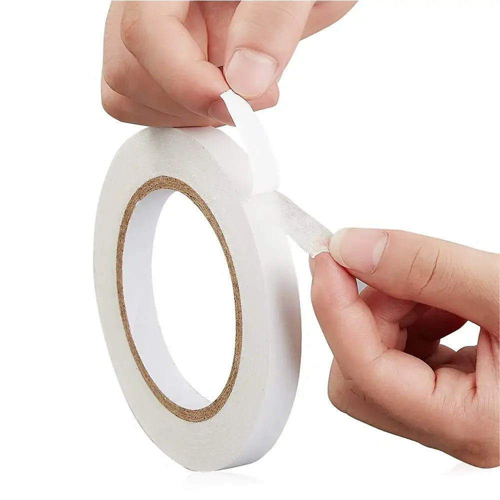 A hand is peeling a white double-sided craft adhesive tape from its roll.