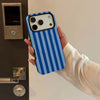 A hand holds a blue and white striped phone case for an iPhone next to a dark appliance.