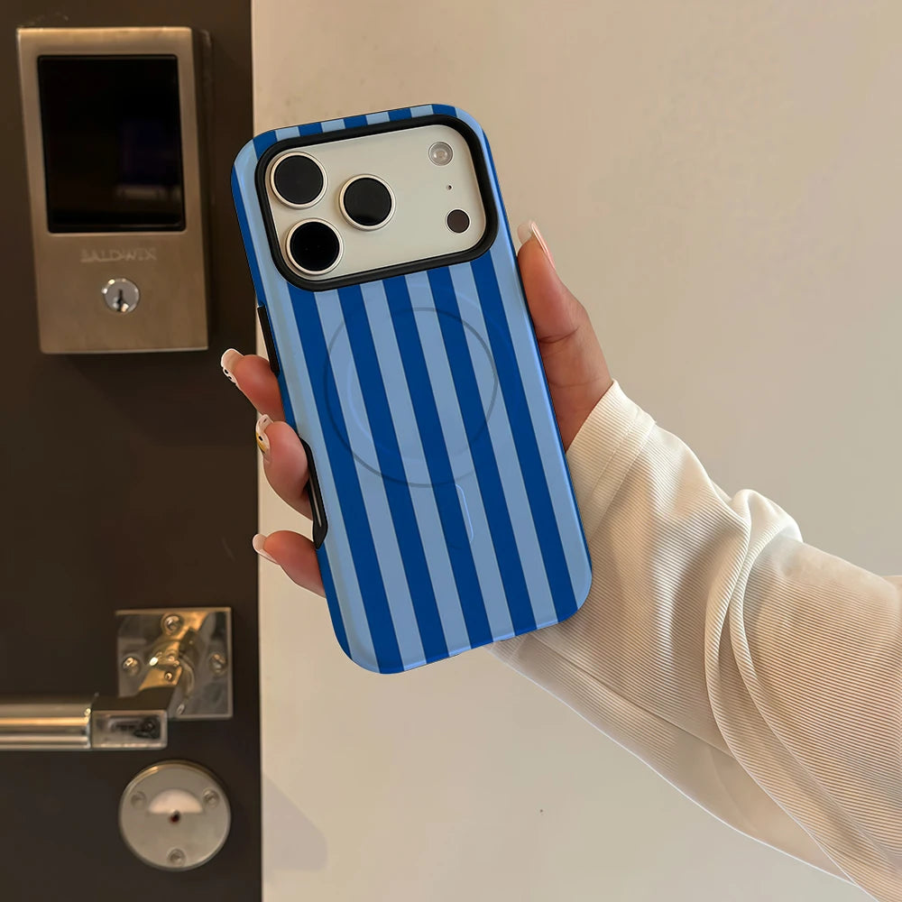 A hand holds a blue and white striped phone case for an iPhone next to a dark appliance.