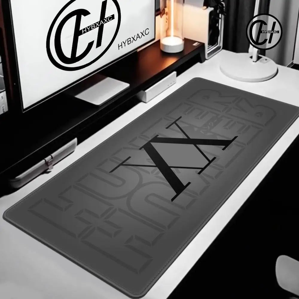 Extra large gaming mouse pad with a black logo placed on a white desk next to a computer monitor.