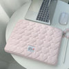 A pink quilted laptop sleeve with a checkered pattern resting on a white table next to a silver laptop.