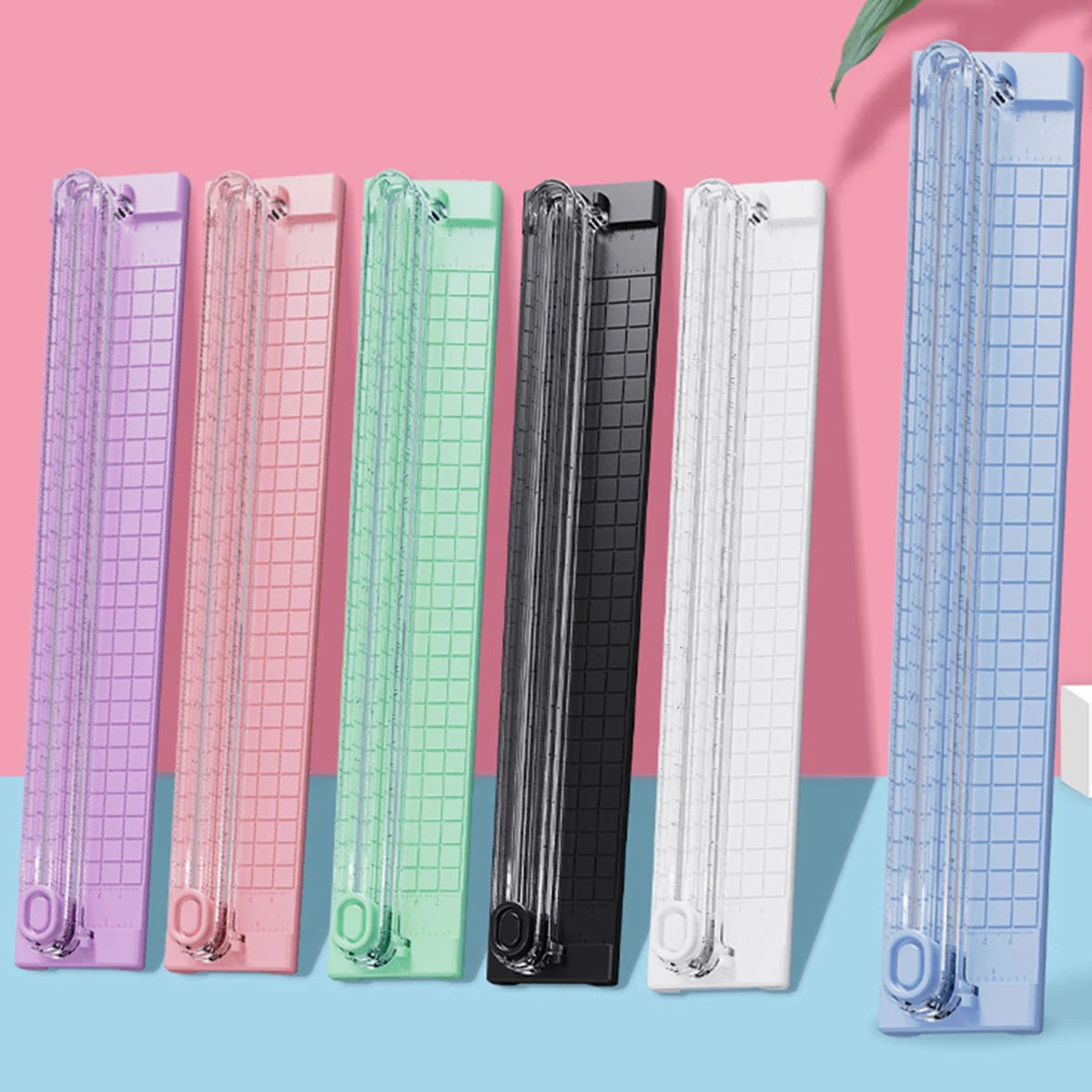 A row of portable manual paper cutters or trimmers in various pastel colors, including purple, pink, mint green, black, and w
