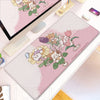 A pink cartoon gaming desk mat featuring cute woodland animals and flowers, displayed next to a laptop.
