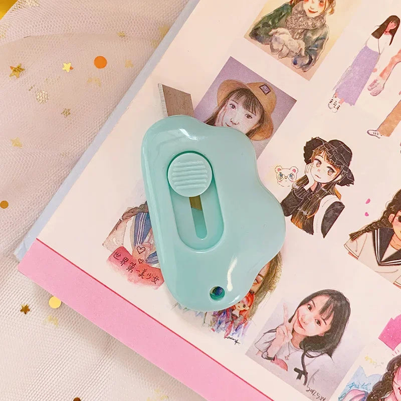 A light blue cat paw mini cutter tool is shown on a pink craft notebook next to illustrations.