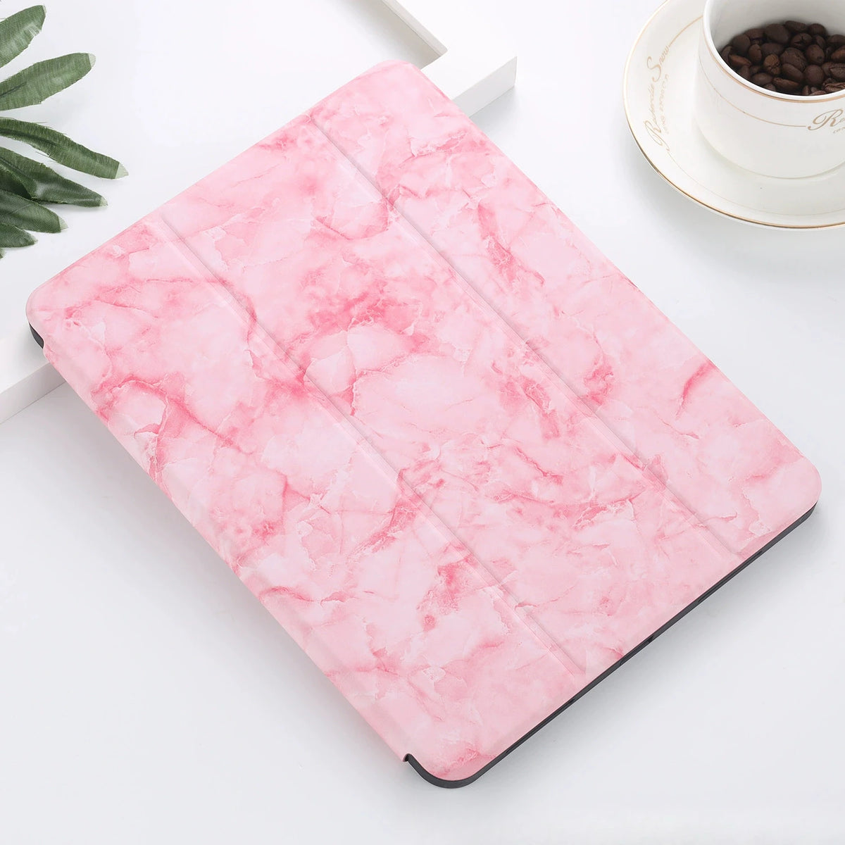 A pink marble patterned skin for an iPad Pro placed on a white surface next to a cup of coffee.