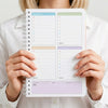 A person holds an A5 daily focus planner notebook with organized sections for priorities, tasks, and notes.