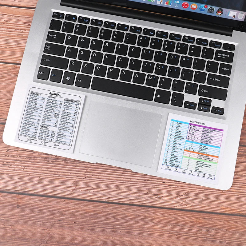 A silver laptop shows a Windows Shortcut Quick Reference sticker on the palm rest area.