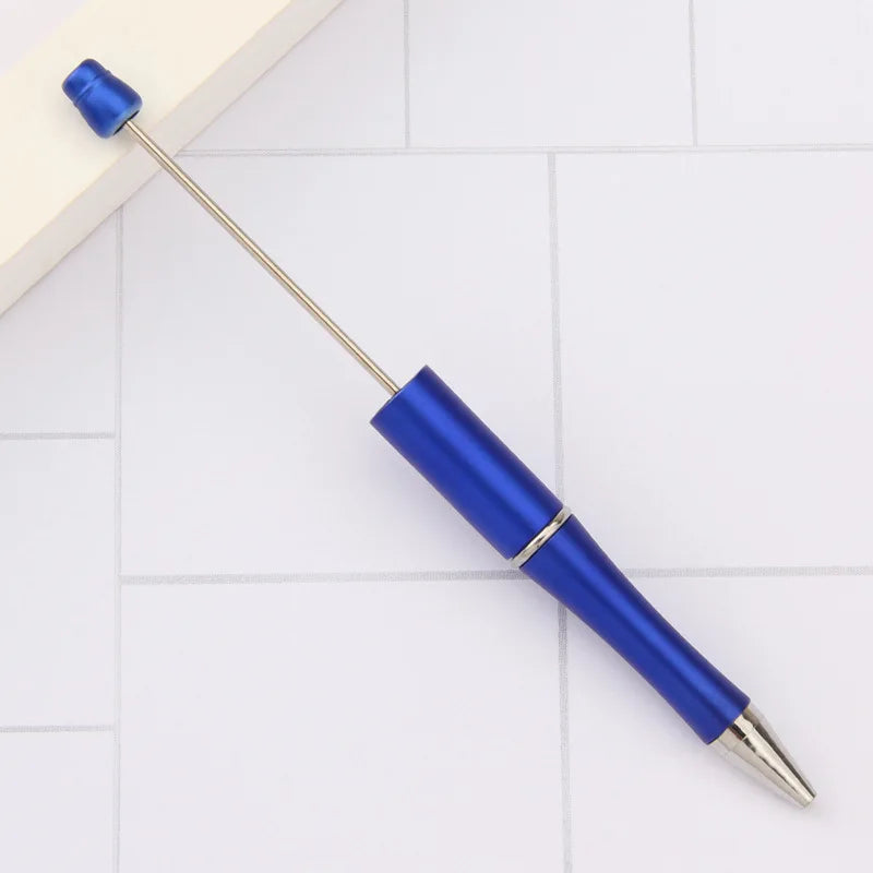 A blue DIY beadable pen with a gold tip is shown on a white tiled surface.