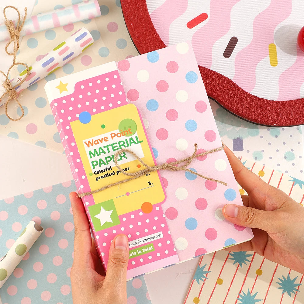 Manos sostienen un papel de scrapbook rosa cuadriculado con puntos y texto colorido, junto a una base roja.
