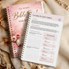 A pink and white guided Bible study journal with a spiral binding and a cover titled 52-Week Bible for Women lies next to a w