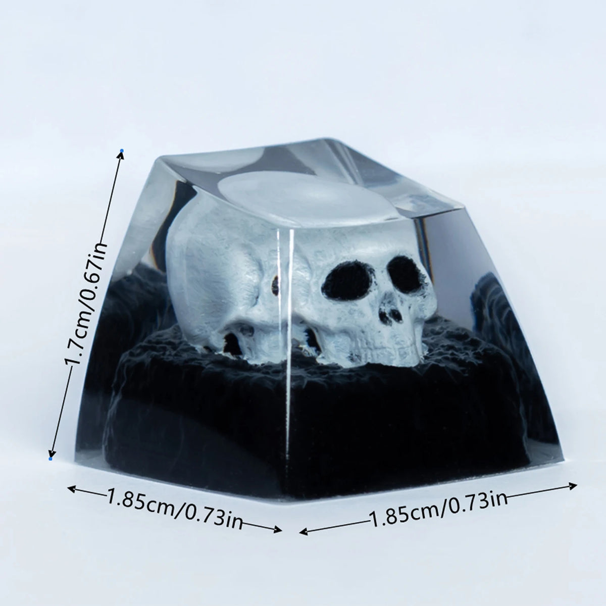 A clear resin mechanical keycap shaped like a monochrome skull resting on a black base.