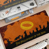 An orange and black desk mat featuring The Fellowship of the Ring design, placed on a wooden desk with gaming accessories.