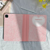 A pink composition book cover with a pencil holder lying on a light gray fabric.