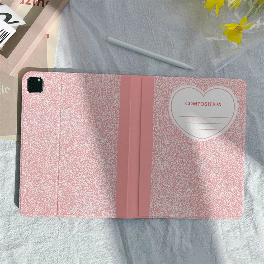 A pink composition book cover with a pencil holder lying on a light gray fabric.