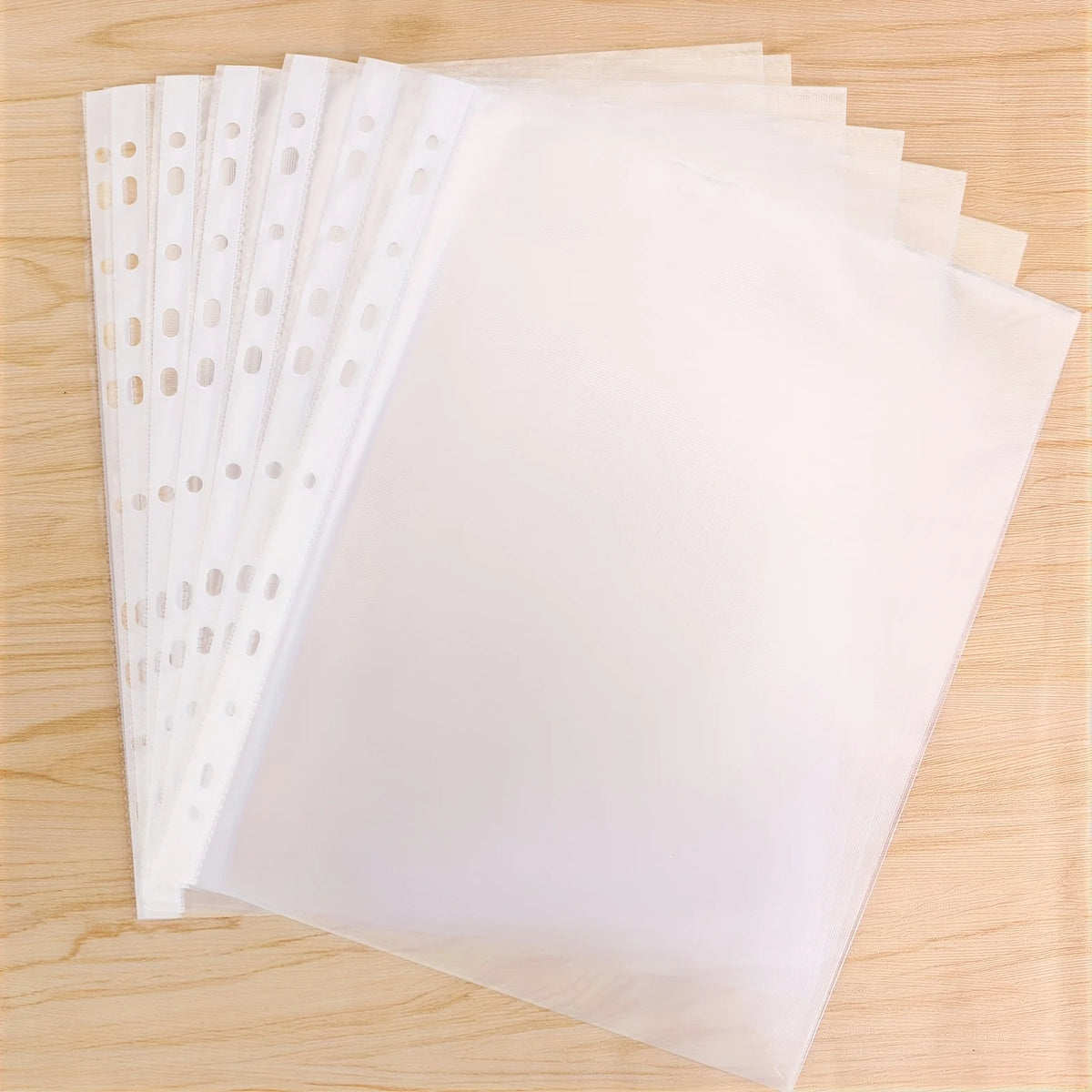 A stack of clear top-loading sheet protectors for 3-ring binders is shown on a wooden surface.