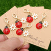 A set of five gold-colored ladybug and daisy keychains are displayed on a brown thank you card.
