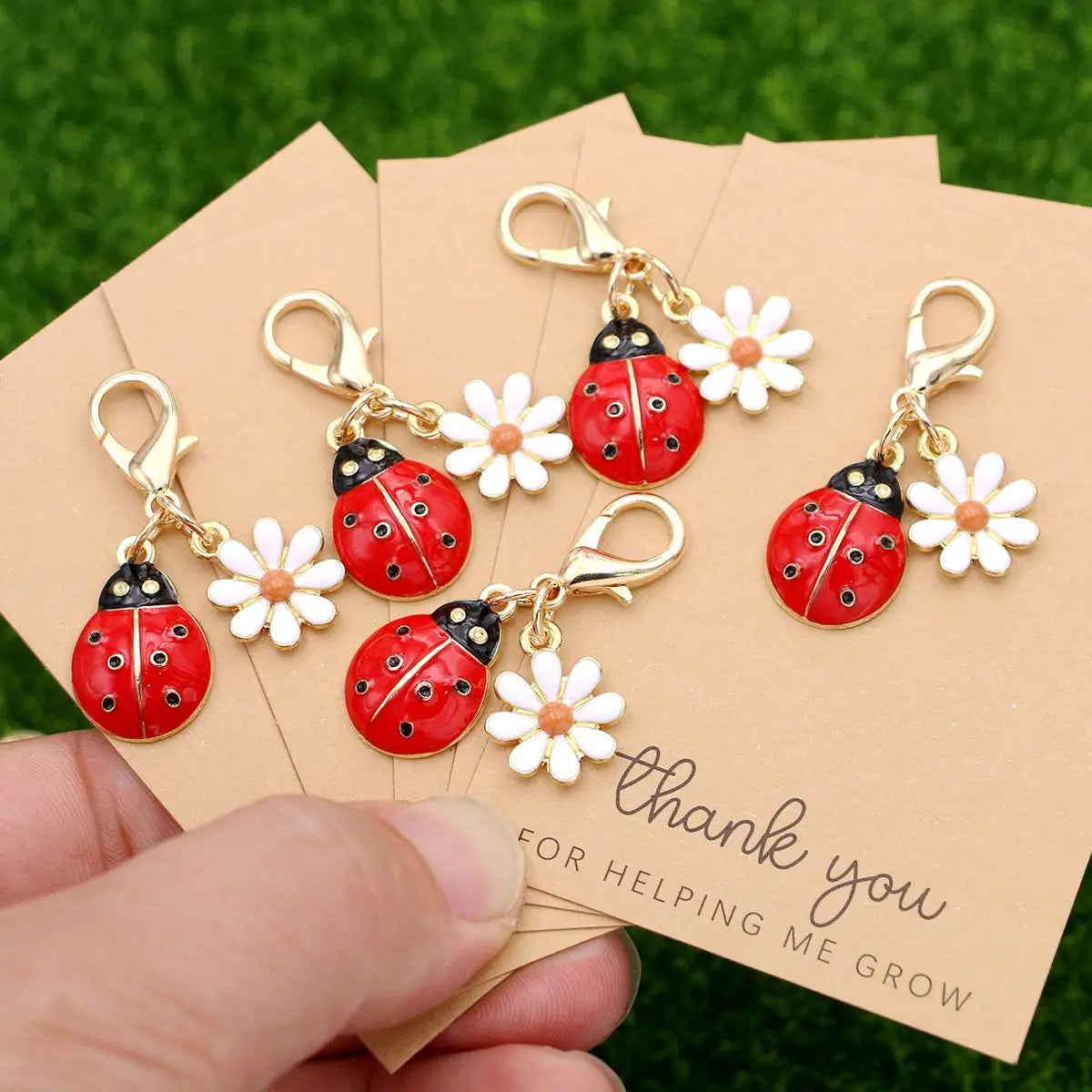 A set of five gold-colored ladybug and daisy keychains are displayed on a brown thank you card.