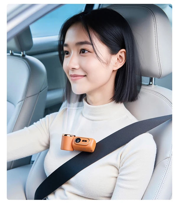 A woman is holding an orange portable rechargeable handheld cooling fan while seated in a car seat.
