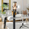A black extendable selfie stick tripod with a wireless remote is displayed in a bright living room setting.
