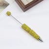 A gold-colored pen accessory featuring a rhinestone-encrusted tip and body, displayed on a white surface.