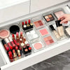 Clear acrylic drawer organizer set containing various makeup products like lipsticks and palettes.