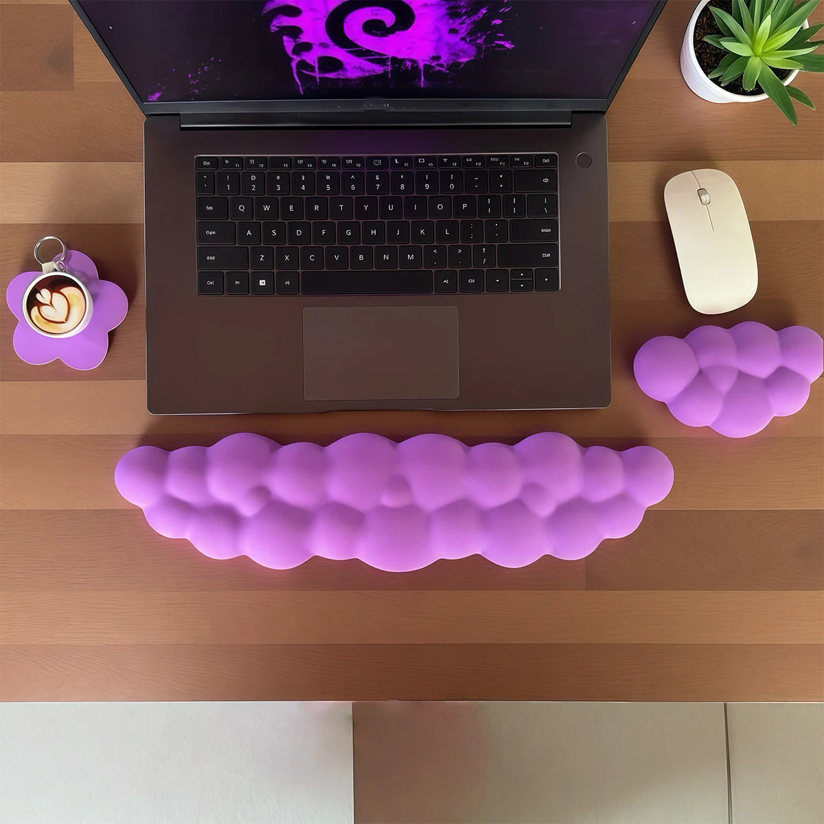Un ordinateur portable sur un bureau en bois avec un repose-poignet clavier nuage violet, une souris et une plante en pot.